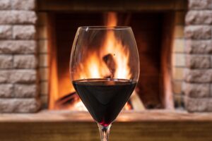 Glass of wine against cozy fireplace background, hygge concept.