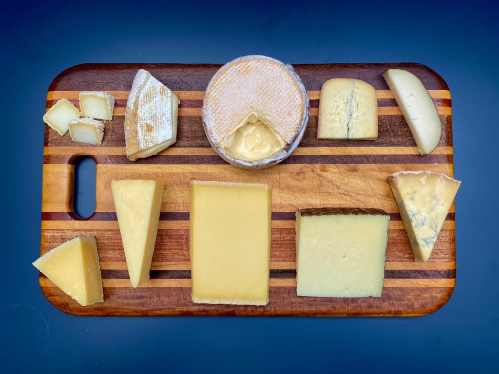 ten selections of cheese on a wood cutting board, seen from above.
