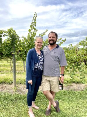 photo of woman and man standing a vineyard.