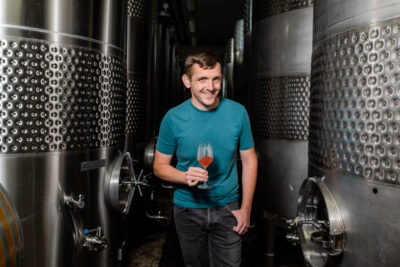 Kelby James Russell, winemaker at Red Newt Cellars. Standing in cellar with glass of red wine.