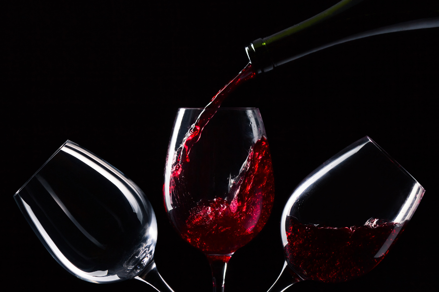 three wine glasses against black background. Red wine is being poured into the center glass.